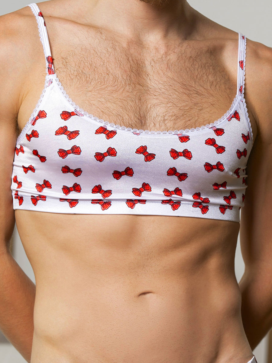 Closeup front view of a man wearing a white satin bra with red bow pattern.