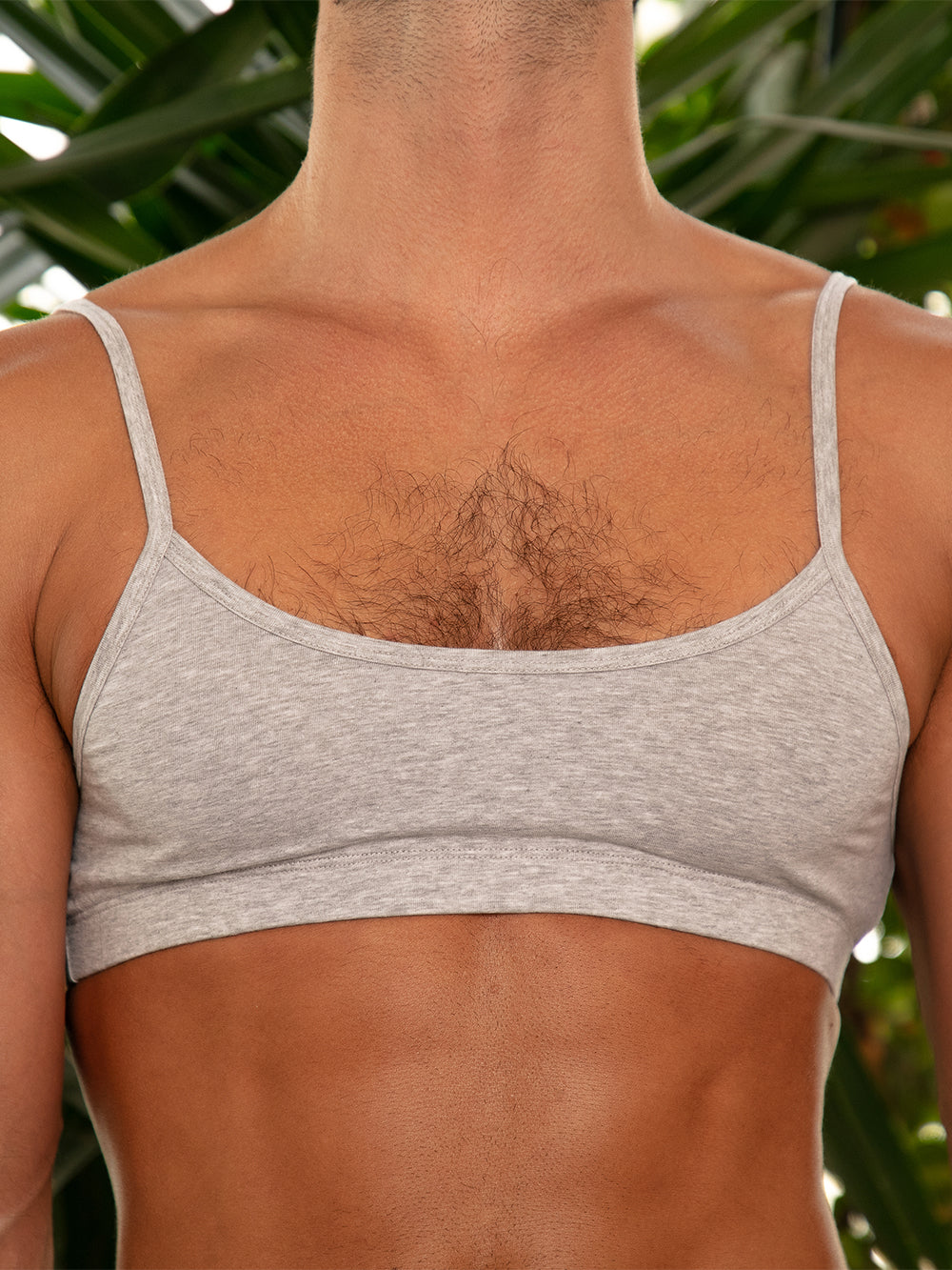 A man wearing a grey sports bra, posing outdoors. 