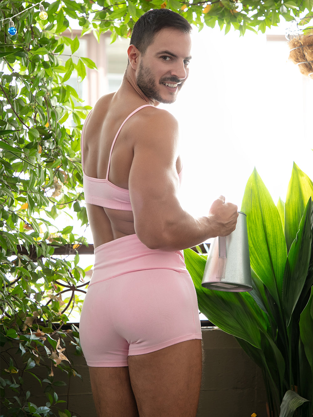 Rear view of a man wearing a matching pink sports bra and athletic shorts, posing outdoors.