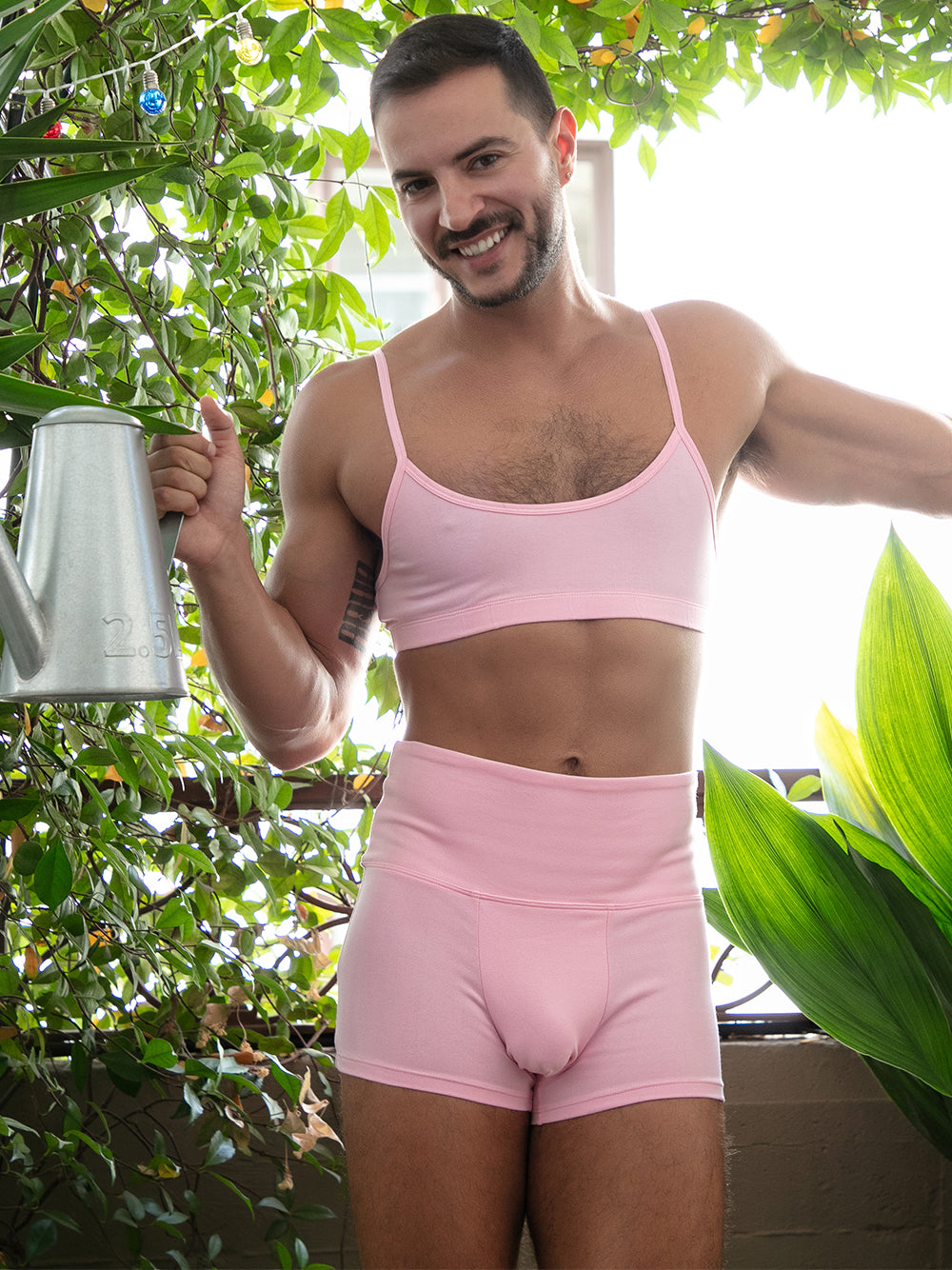 A man wearing a matching pink sports bra and athletic shorts, posing outdoors.