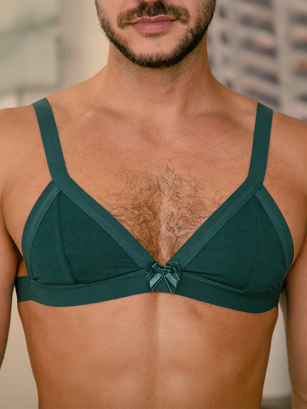 Closeup view of a man wearing a teal green bra with matching bow.