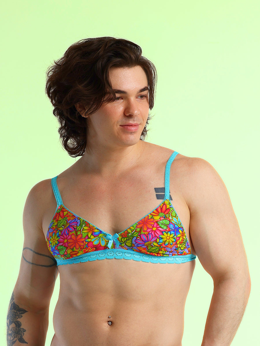 A man wearing a rainbow floral pattern bra with light blue lace details, against a green background.