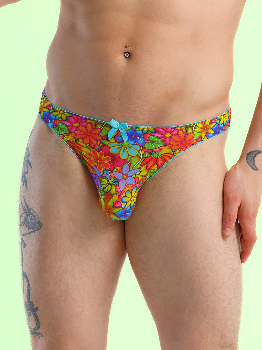 Closeup view of a man wearing a floral print thong panty with a blue bow, against a green background.