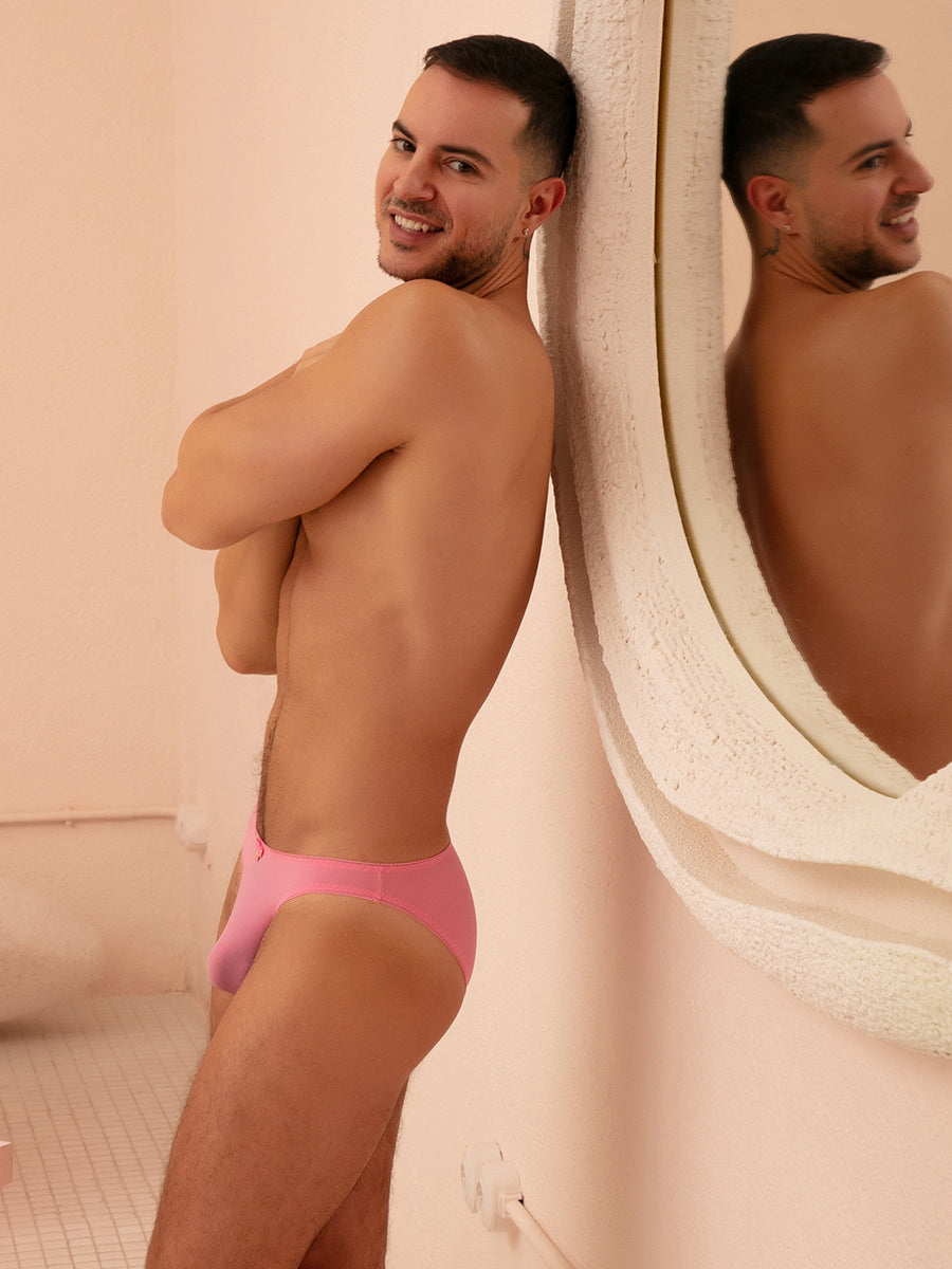 Side view of man wearing pink XDress panties with matching bow, standing next to a mirror.