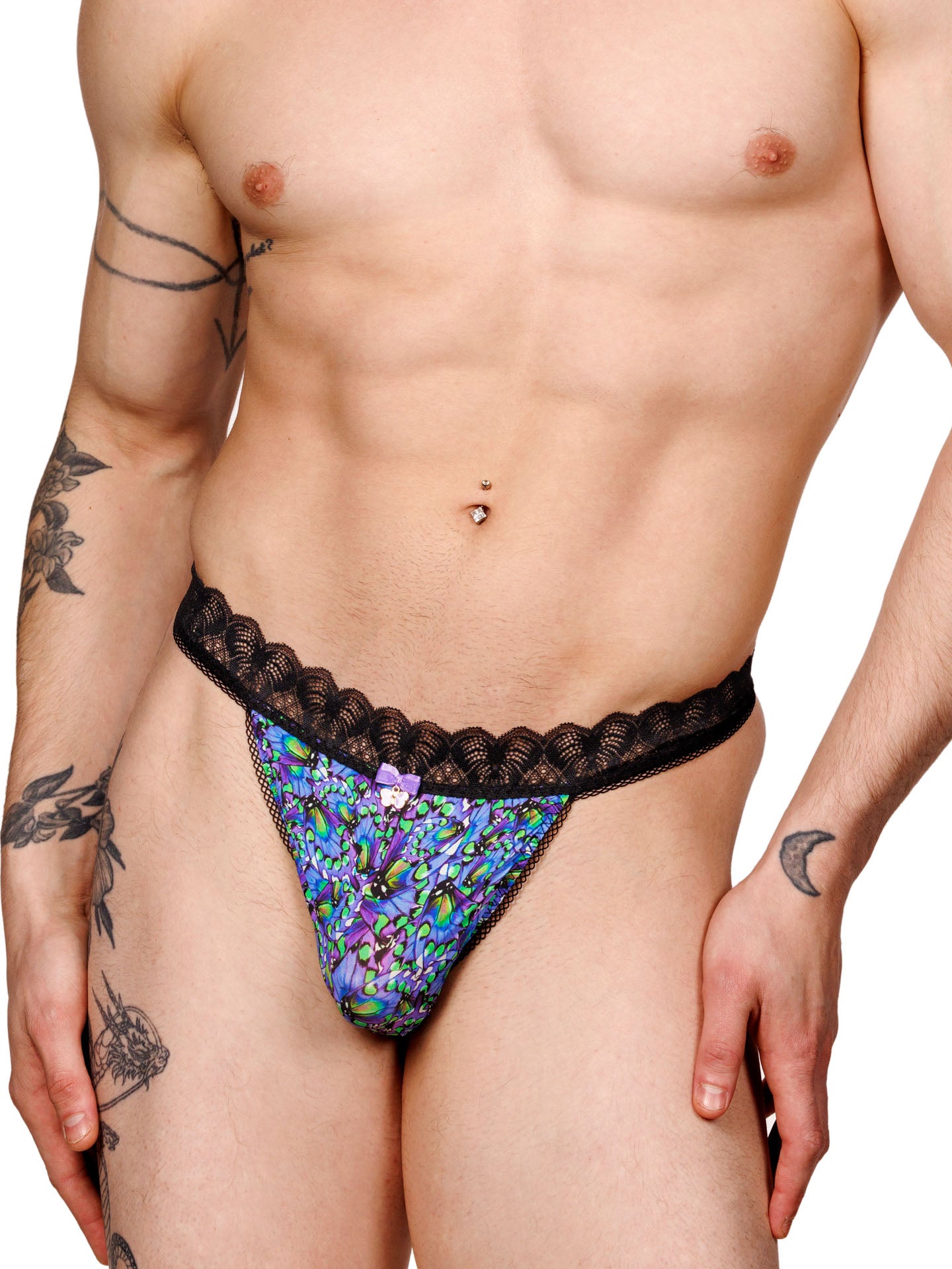 Male model wearing a blue floral print men's thong with a black lace waistband and metallic charm at the front, shown from the front.