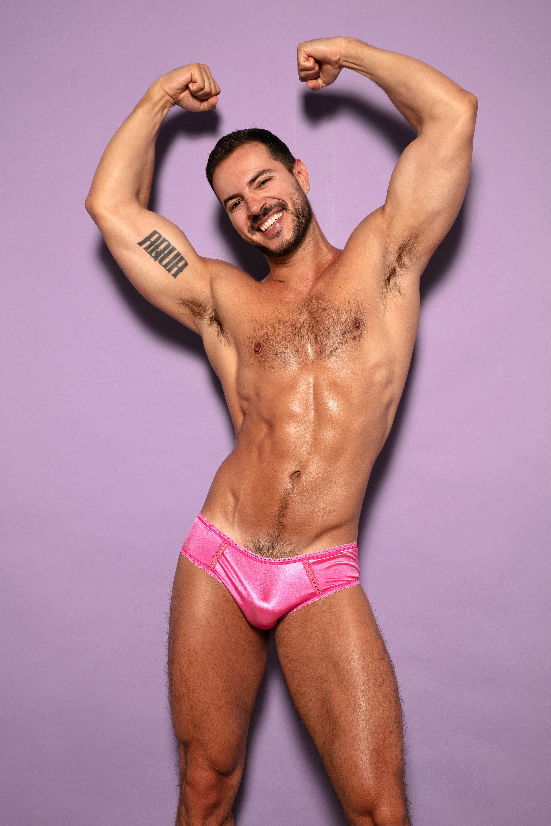 Front view of a man wearing pink satin panties with his arms above his head.
