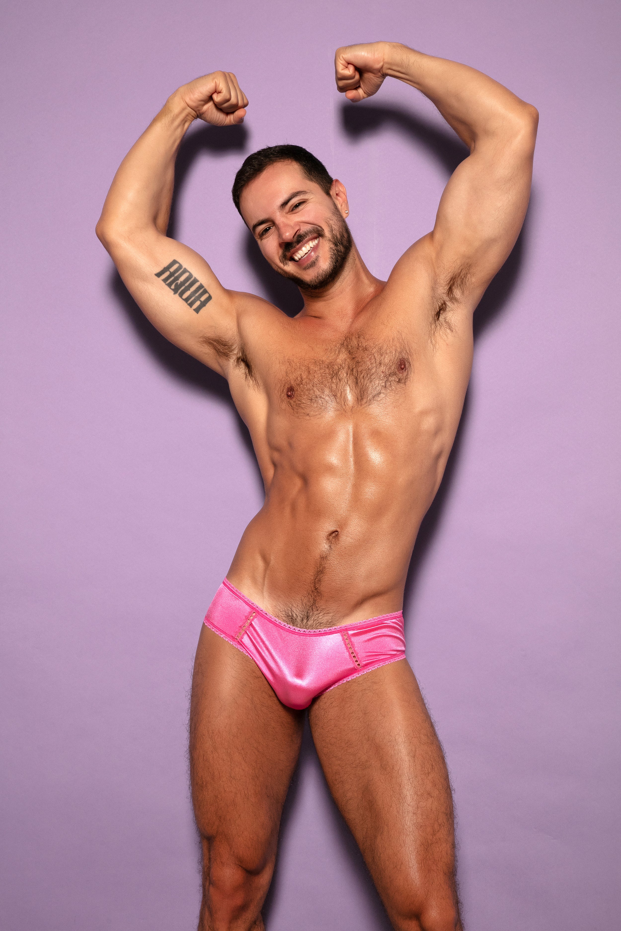 Front view of a man wearing pink satin panties with his arms above his head.