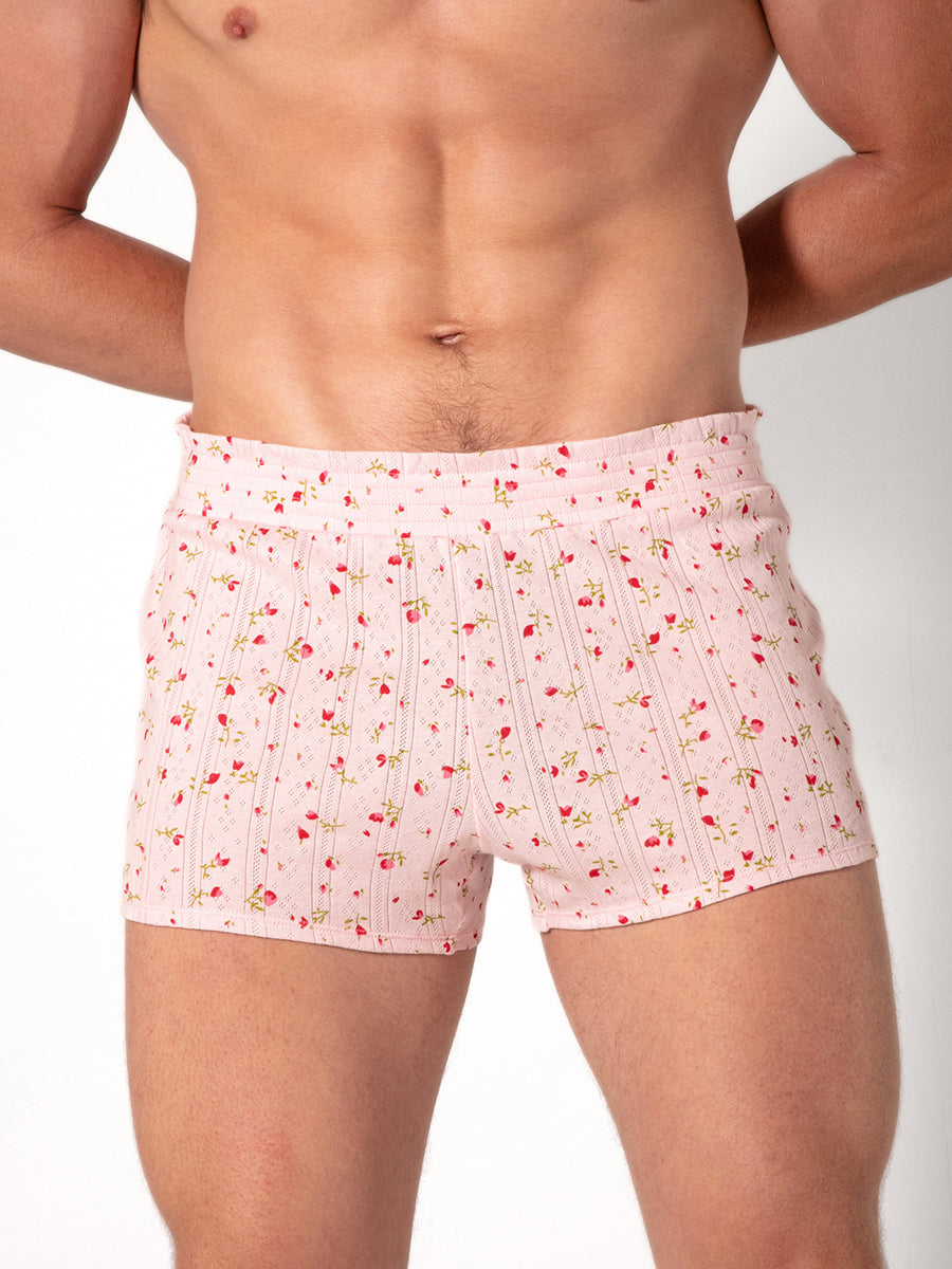 Man wearing pink shorts with a red floral pattern on a plain background