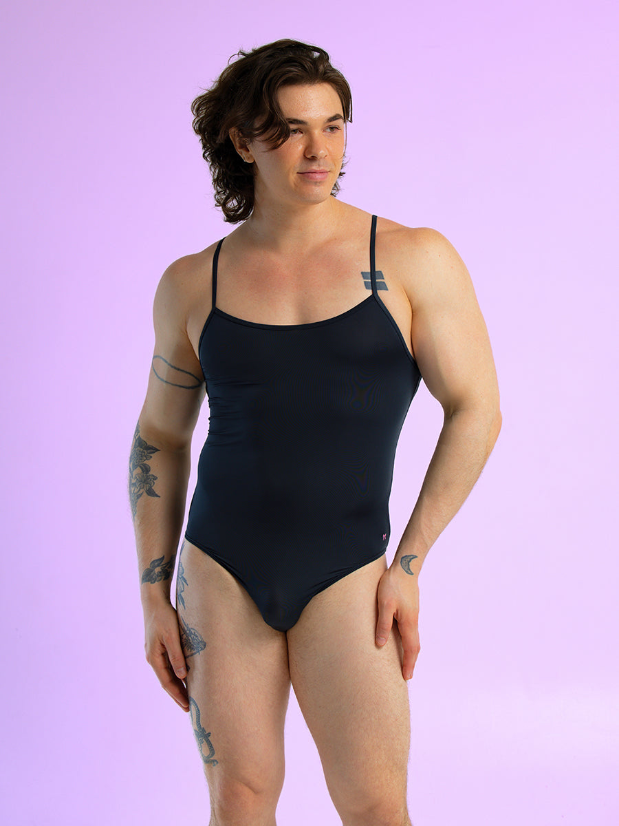 Front view of a man wearing a black bodysuit with thin shoulder straps, against a purple background.