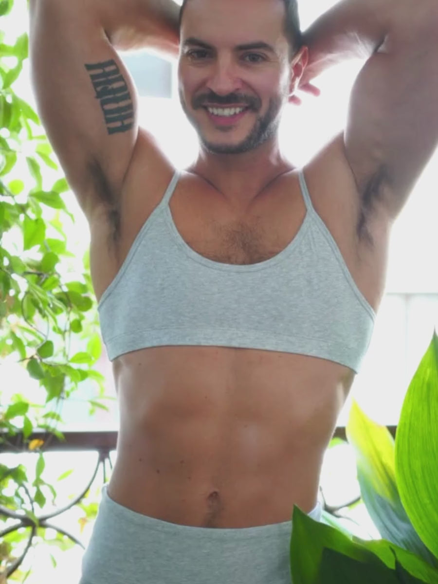 A man wearing matching grey athletic shorts and sports bra, posing outdoors.